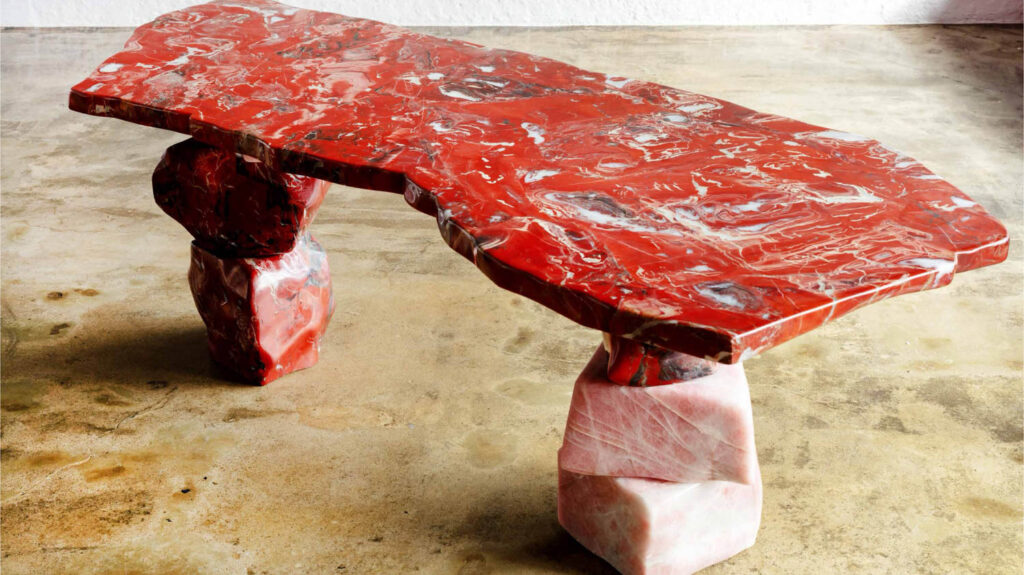 A table with a slab of red marbled stone supported by stacked blocks of red and pale pink stone.