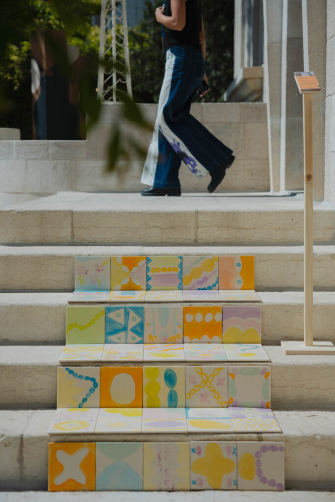 A person in patterned jeans walks past stone stairs decorated with rows of hand-painted ceramic tiles.
