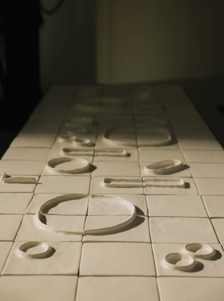 A grid of square white ceramic tiles featuring shallow, raised circular and rectangular shapes.