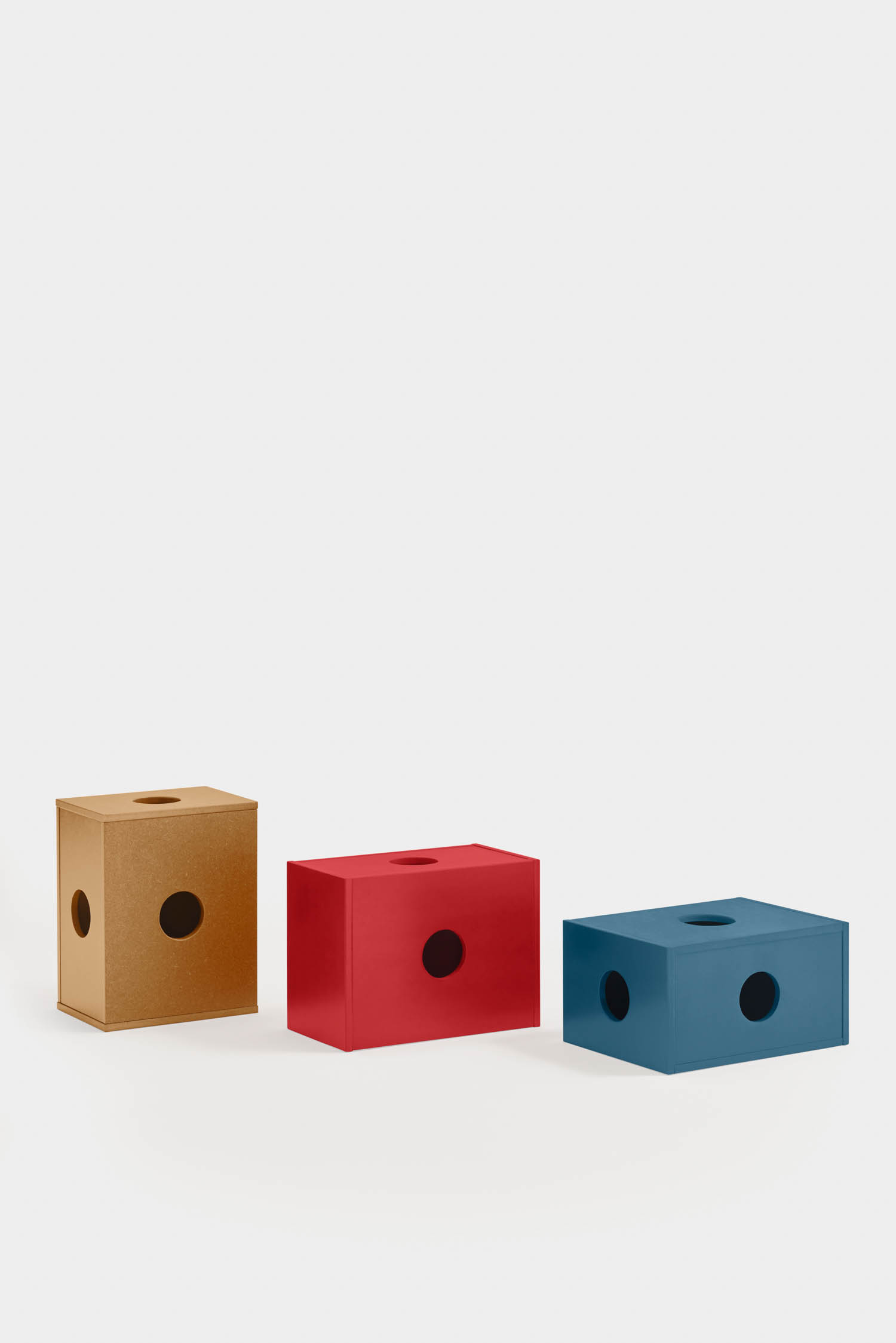 Three rectangular boxes—brown, red, and blue—each with a circular hole on the side and top, are arranged against a plain white background.