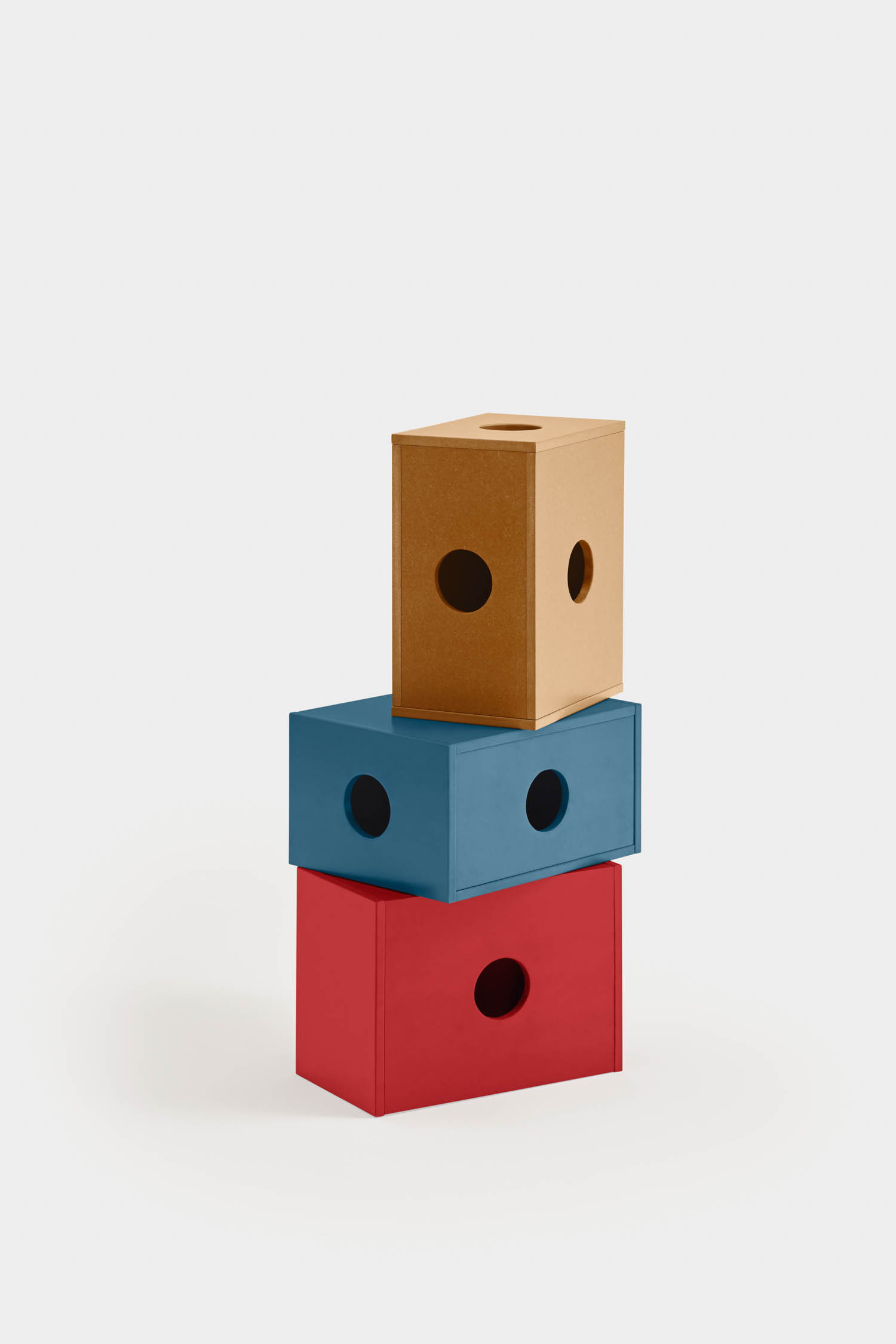 Three rectangular boxes with circular holes are stacked vertically; the bottom box is red, the middle is blue, and the top is brown, all against a plain white background.