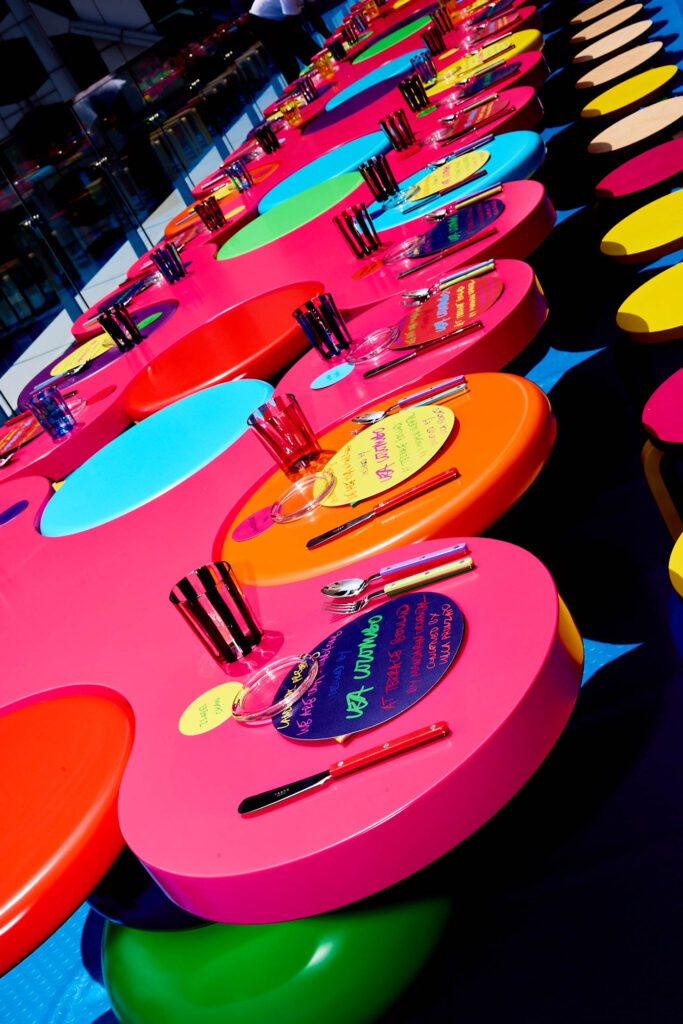 Rows of brightly colored, circular tables set with glasses and place cards for a formal event.