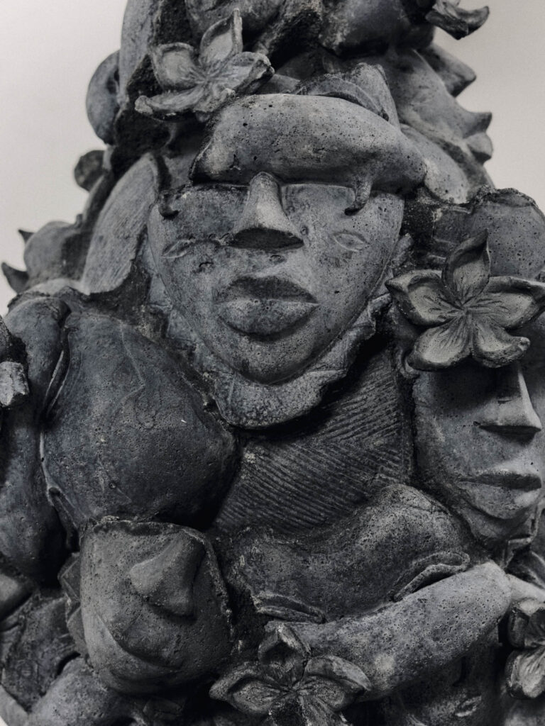 A stone sculpture featuring multiple carved human faces integrated with floral and leaf motifs.
