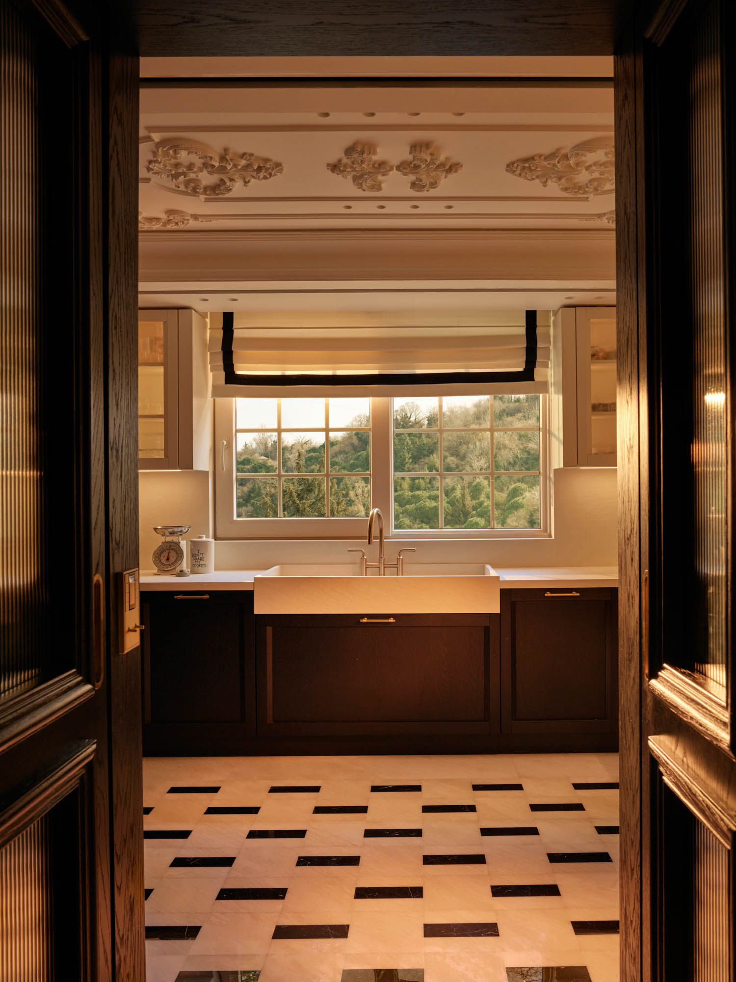 View through a doorway into a kitchen with dark cabinetry, a white farmhouse sink, and black and white checkered flooring.