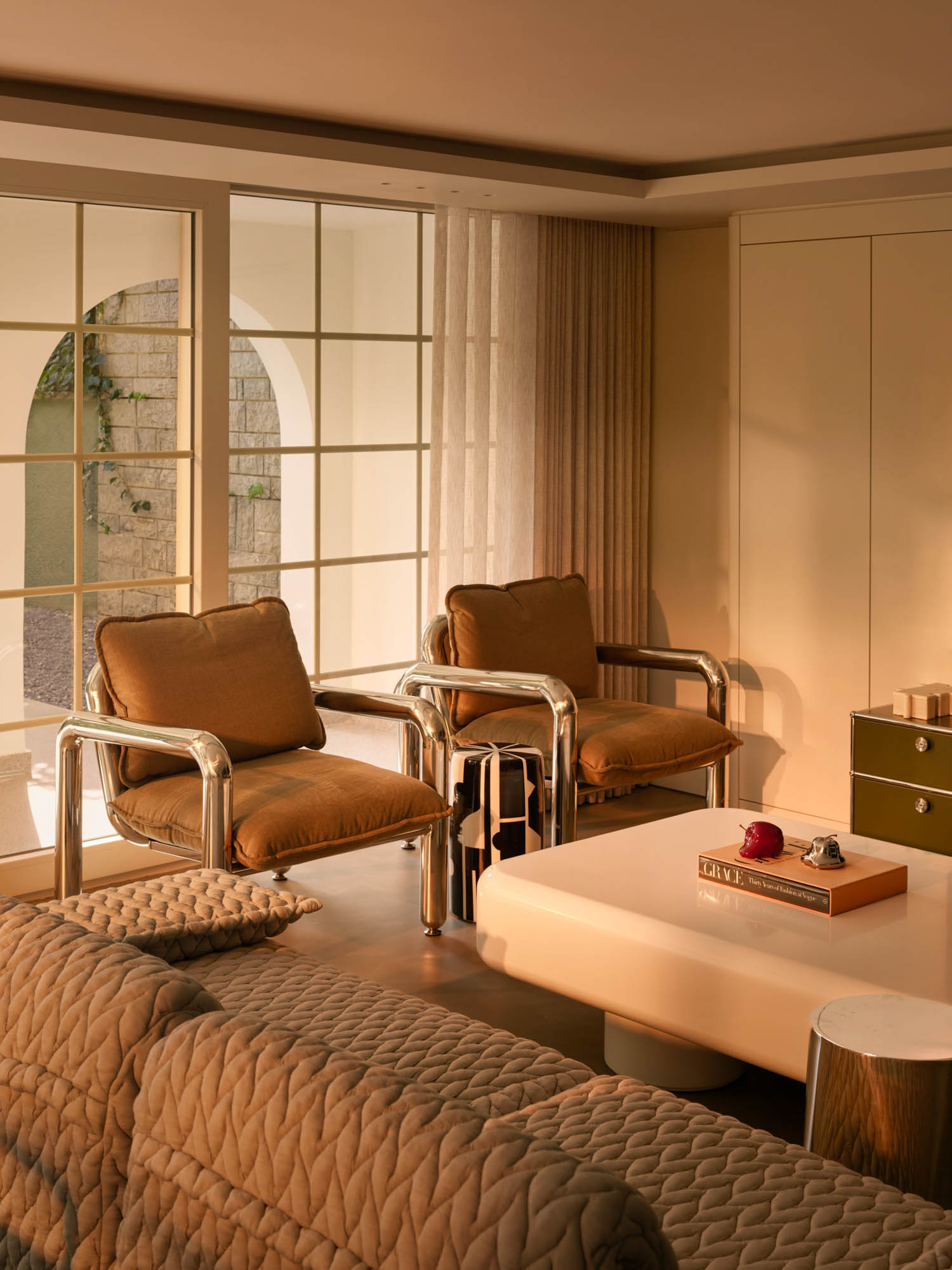 Two brown armchairs with chrome frames positioned in front of large windows, with a coffee table in the foreground.