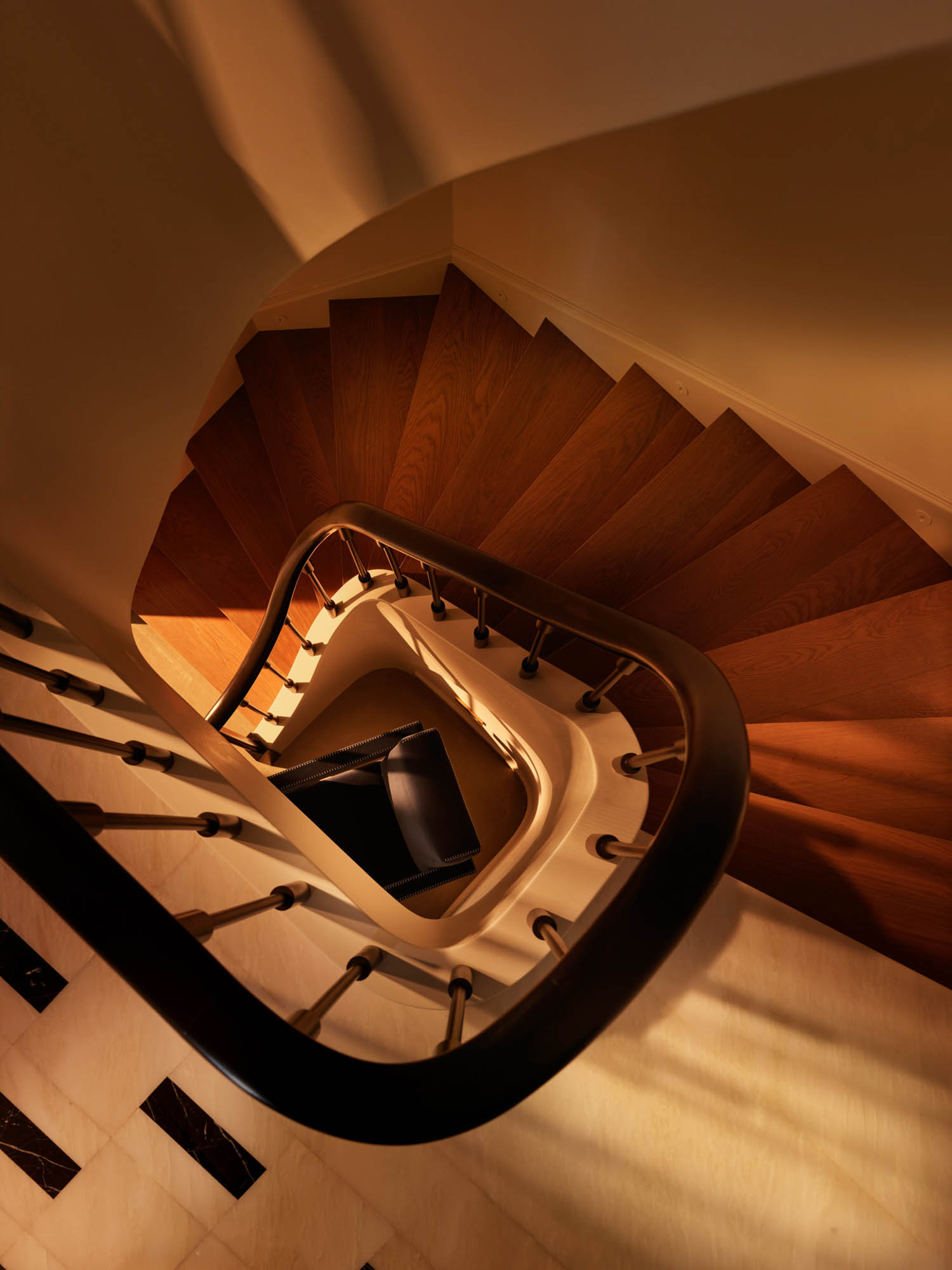 A high-angle view looking down a wooden spiral staircase with a dark handrail.