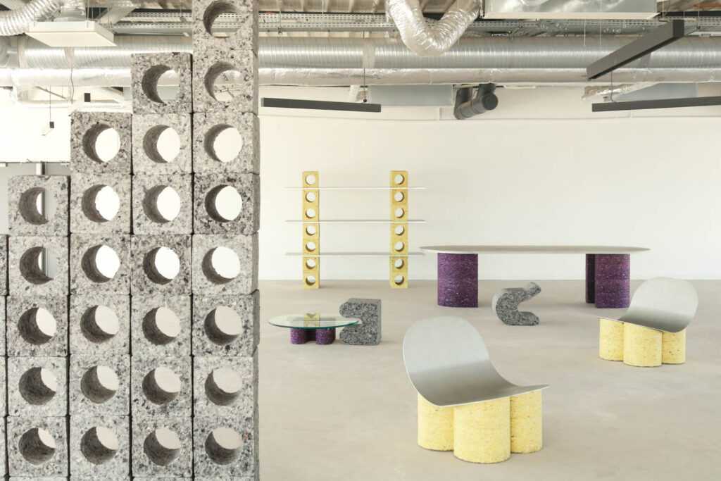 A showroom featuring furniture made from industrial blocks and metal, including shelves, a dining table, a coffee table, and curved chairs.