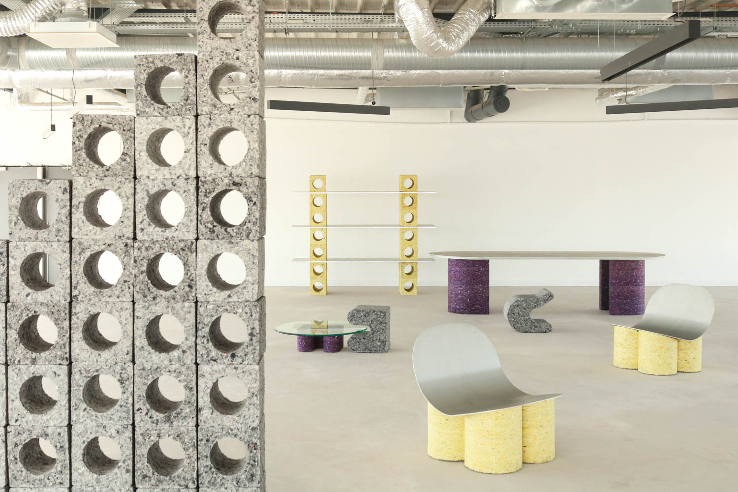 A showroom featuring furniture made from industrial blocks and metal, including shelves, a dining table, a coffee table, and curved chairs.