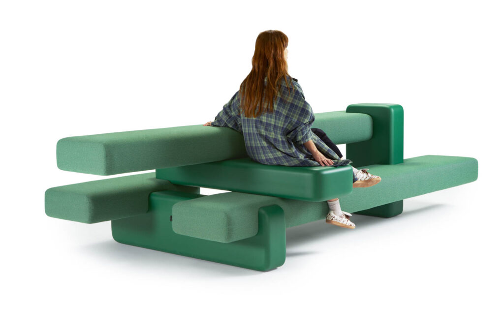 A person sits on a modern green bench with layered, rectangular cushions against a white background.