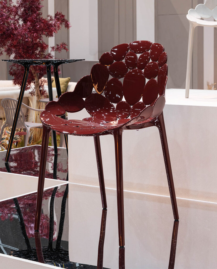 A modern chair with a glossy, dark red, circular-patterned seat and backrest is displayed on a platform indoors.