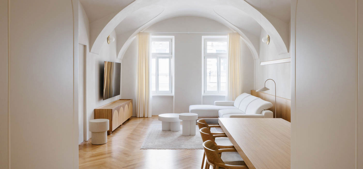 A minimalist living and dining space with arched ceilings, white furniture, and light wood flooring.