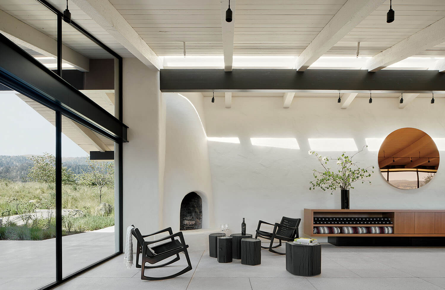 Living room with two black rocking chairs, three dark wood side tables, a fireplace, and a low console cabinet with a circular mirror above.