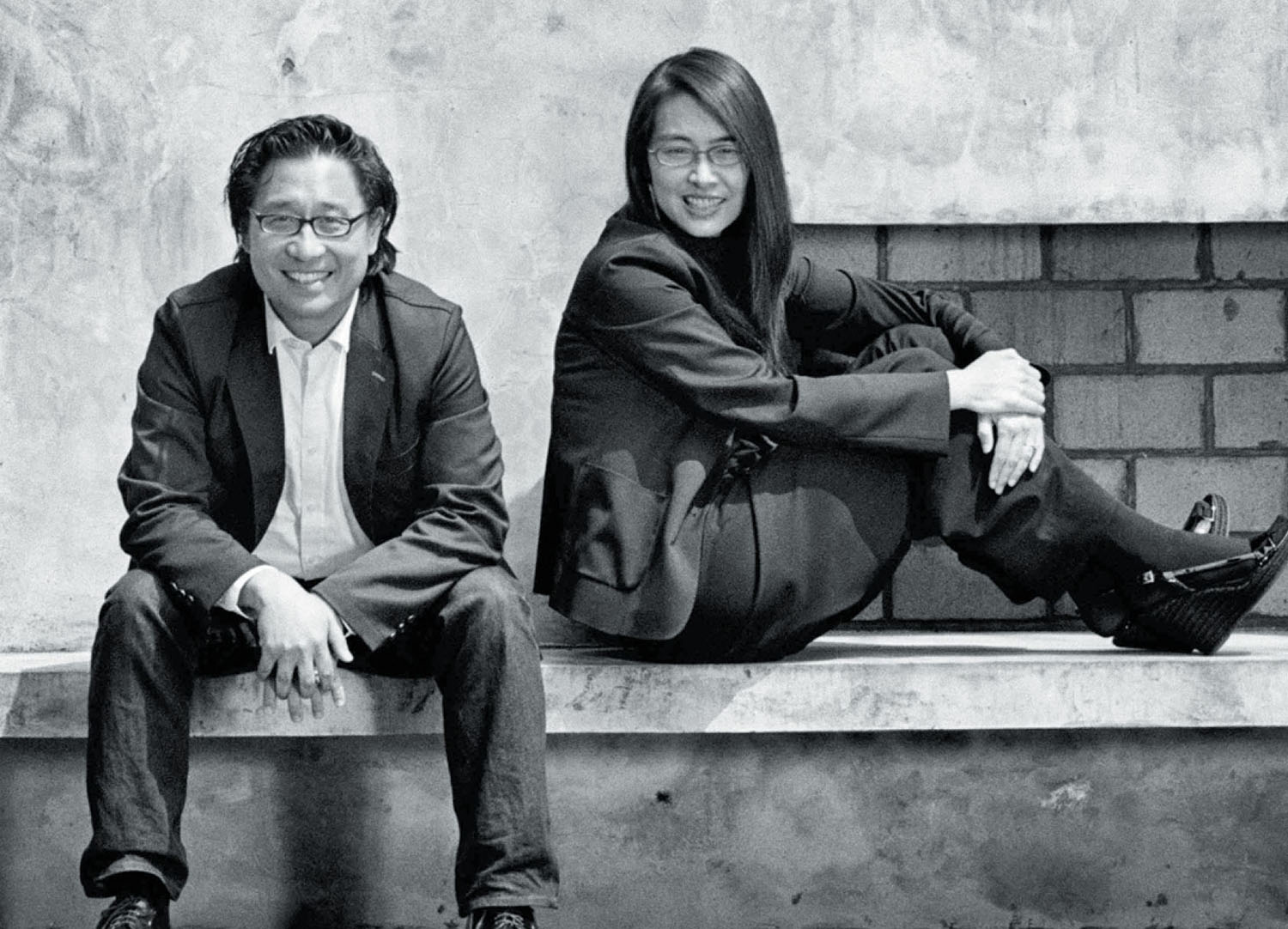A man and a woman in business casual attire sitting side-by-side on a concrete ledge.