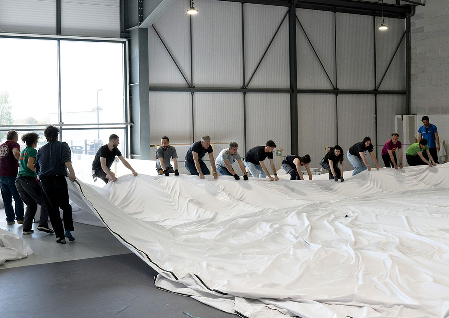 A group of people working together to unfold a large white tarp inside a warehouse.