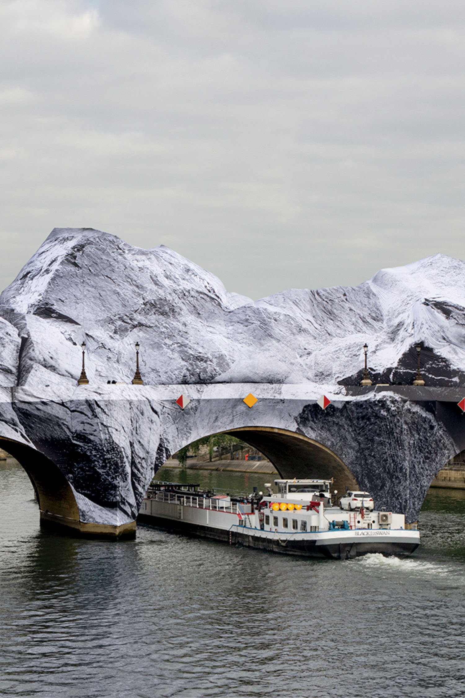 A river barge named Black Swan passing under a bridge wrapped in a large mountain-scape image.