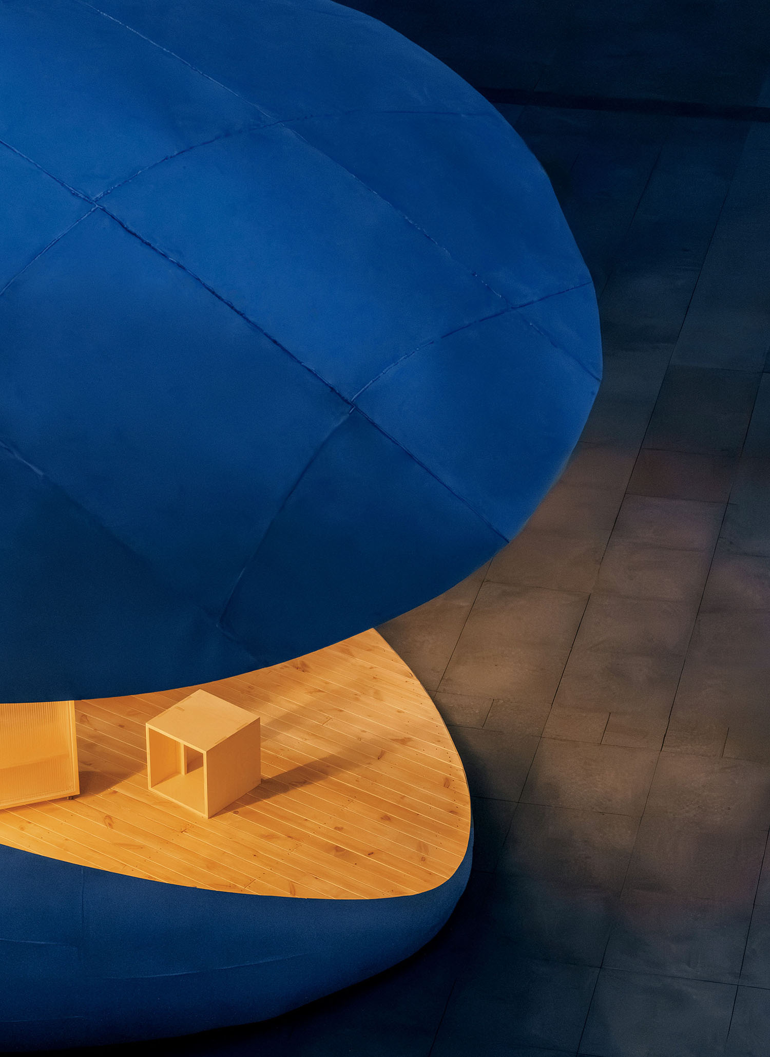 A blue, rounded, segmented structure positioned above a curved wooden platform with small wooden cube stools.