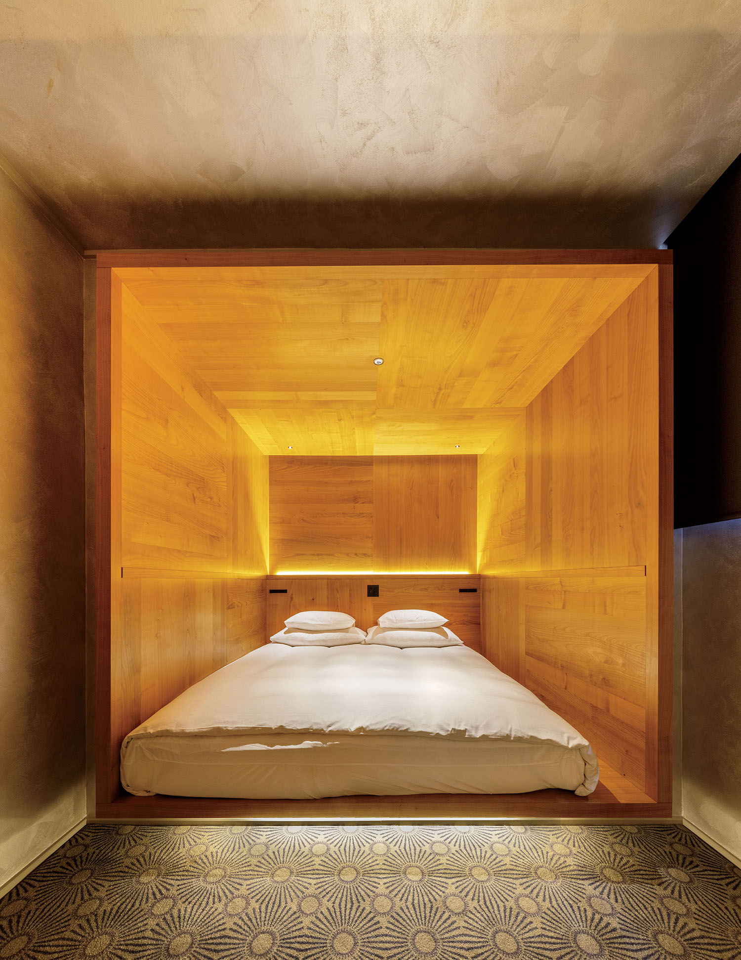A double bed nestled inside a wooden alcove with integrated lighting.