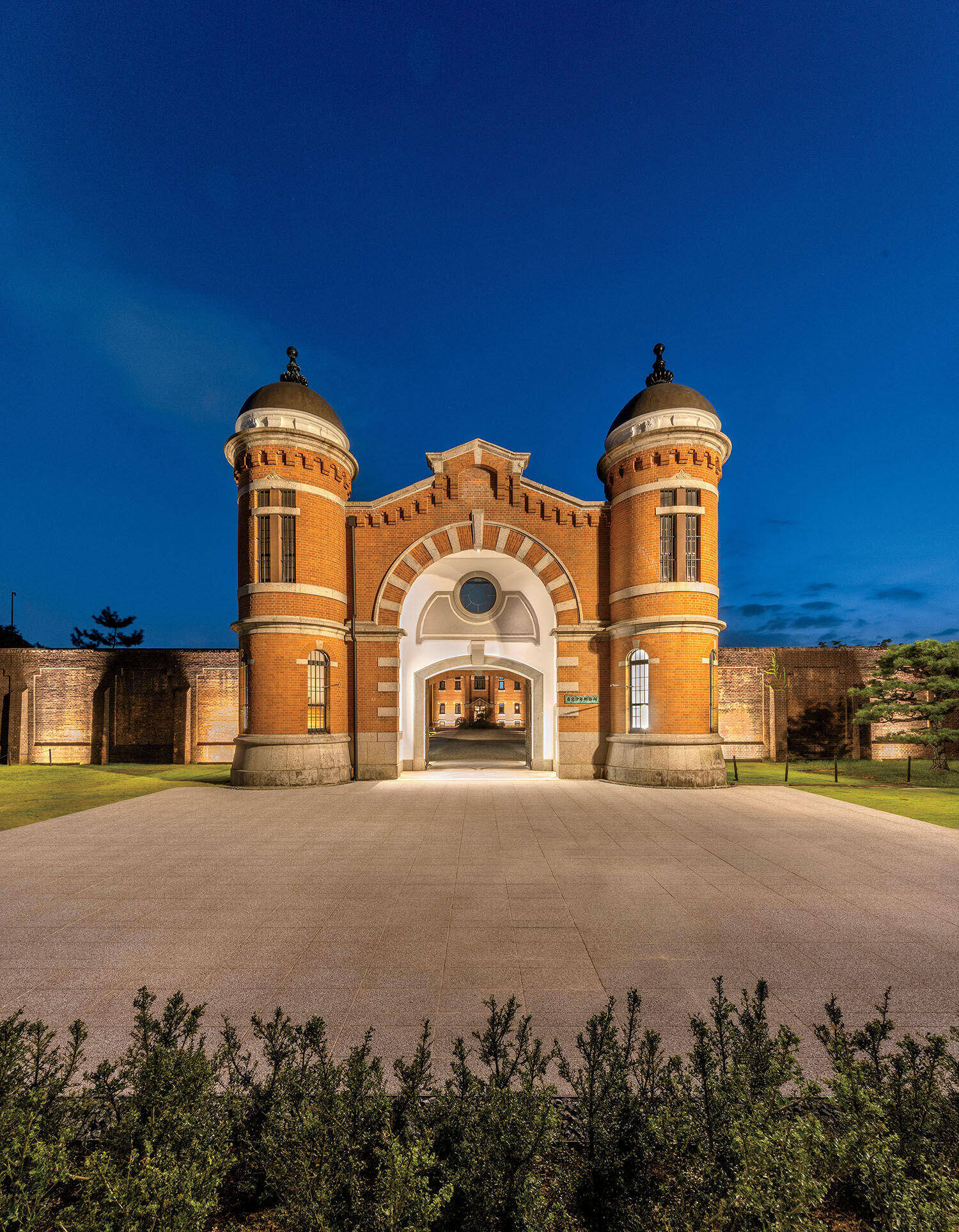 The historic red brick gate of the Nara Prison, featuring two symmetrical towers and a central arched entrance at twilight.