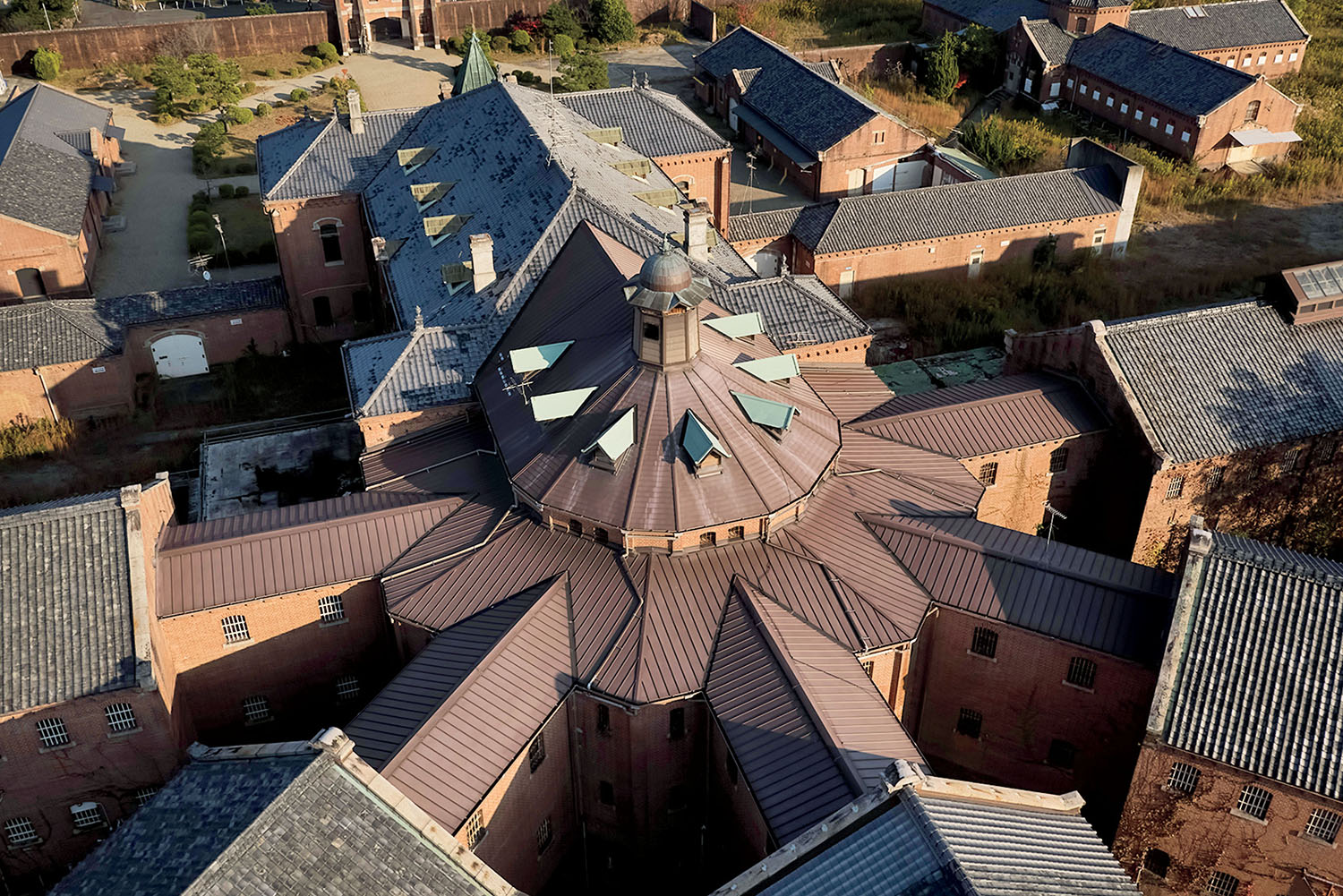 Aerial view of a historic prison complex with a central circular hub and radiating wings of brick buildings with tiled roofs.