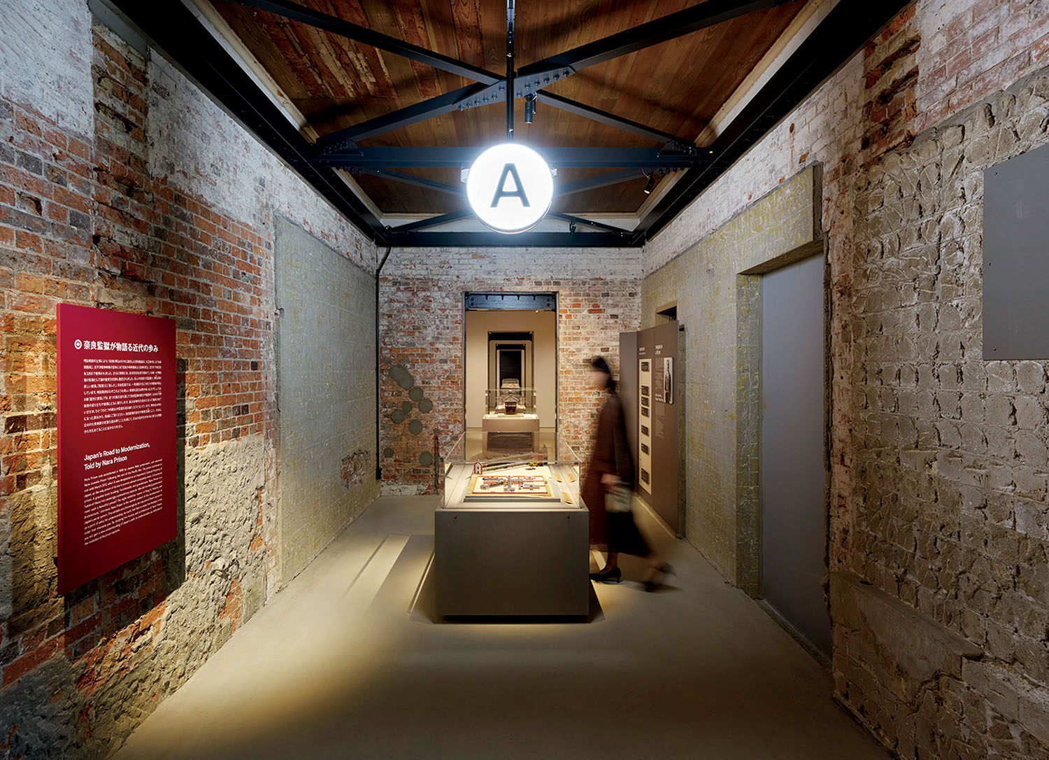 A hallway in an old brick building with a red information sign, a central display case, and an overhead sign marked with the letter A.