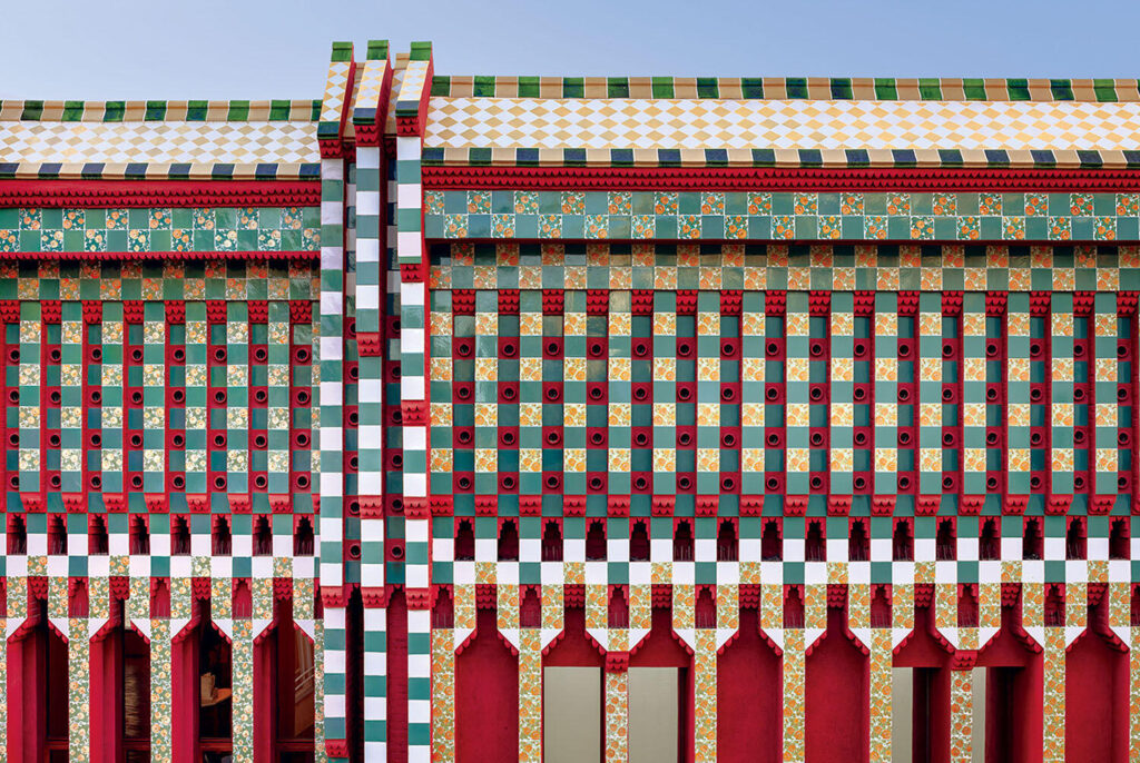 The facade of Casa Vicens, featuring a repetitive pattern of green and white tiles with floral motifs and red structural pillars.
