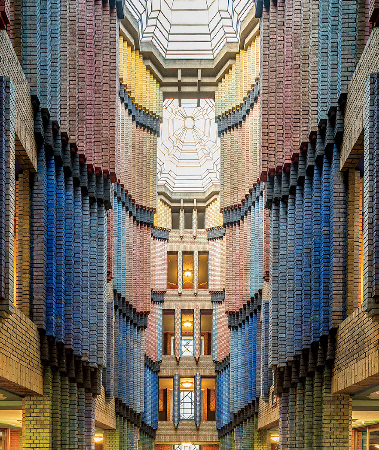 A multi-story atrium with walls made of patterned, multi-colored bricks rising toward a geometric glass ceiling.