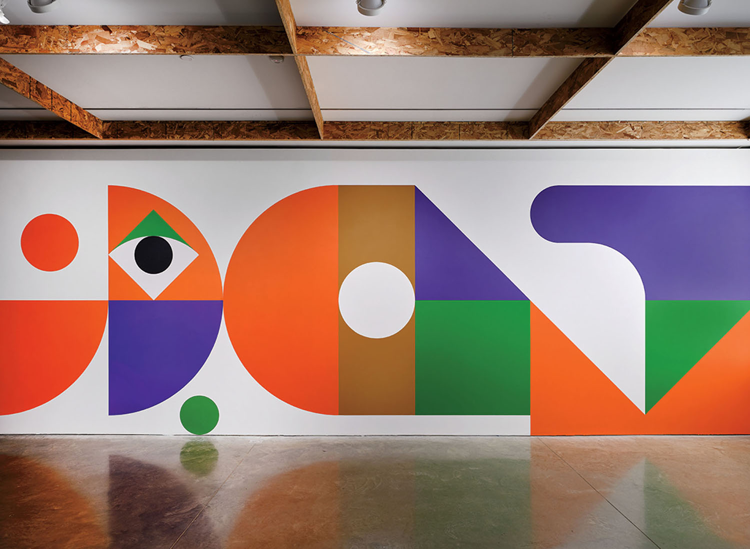 A large wall mural featuring colorful geometric shapes, including circles, triangles, and abstract blocks in orange, purple, green, brown, and white.