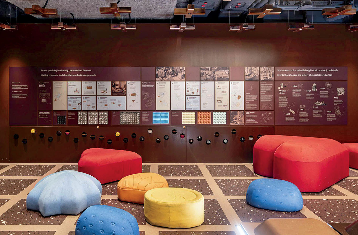 An exhibit wall about chocolate production featuring informational panels, with colorful, rounded floor cushions in the foreground.