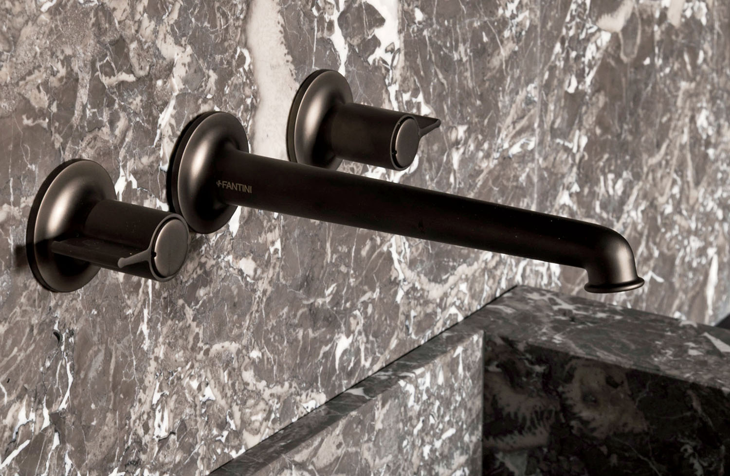 Wall-mounted dark metal bathroom faucet with two handles, installed on a gray marble surface.