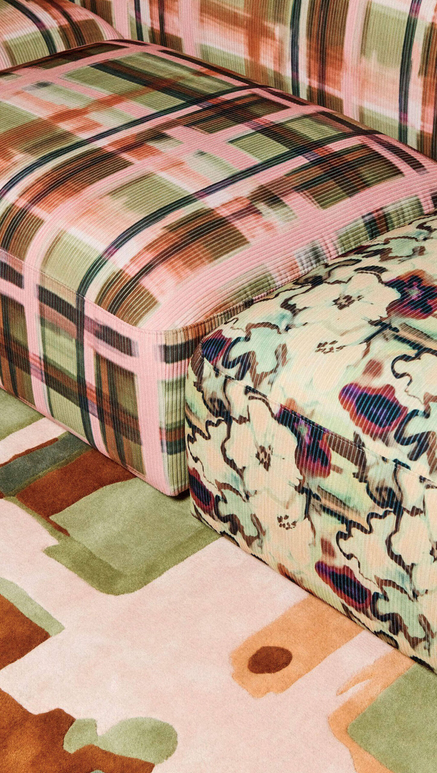 Two upholstered ottomans, one with a green and pink plaid pattern and the other with a dark abstract floral print, sitting on a patterned rug.