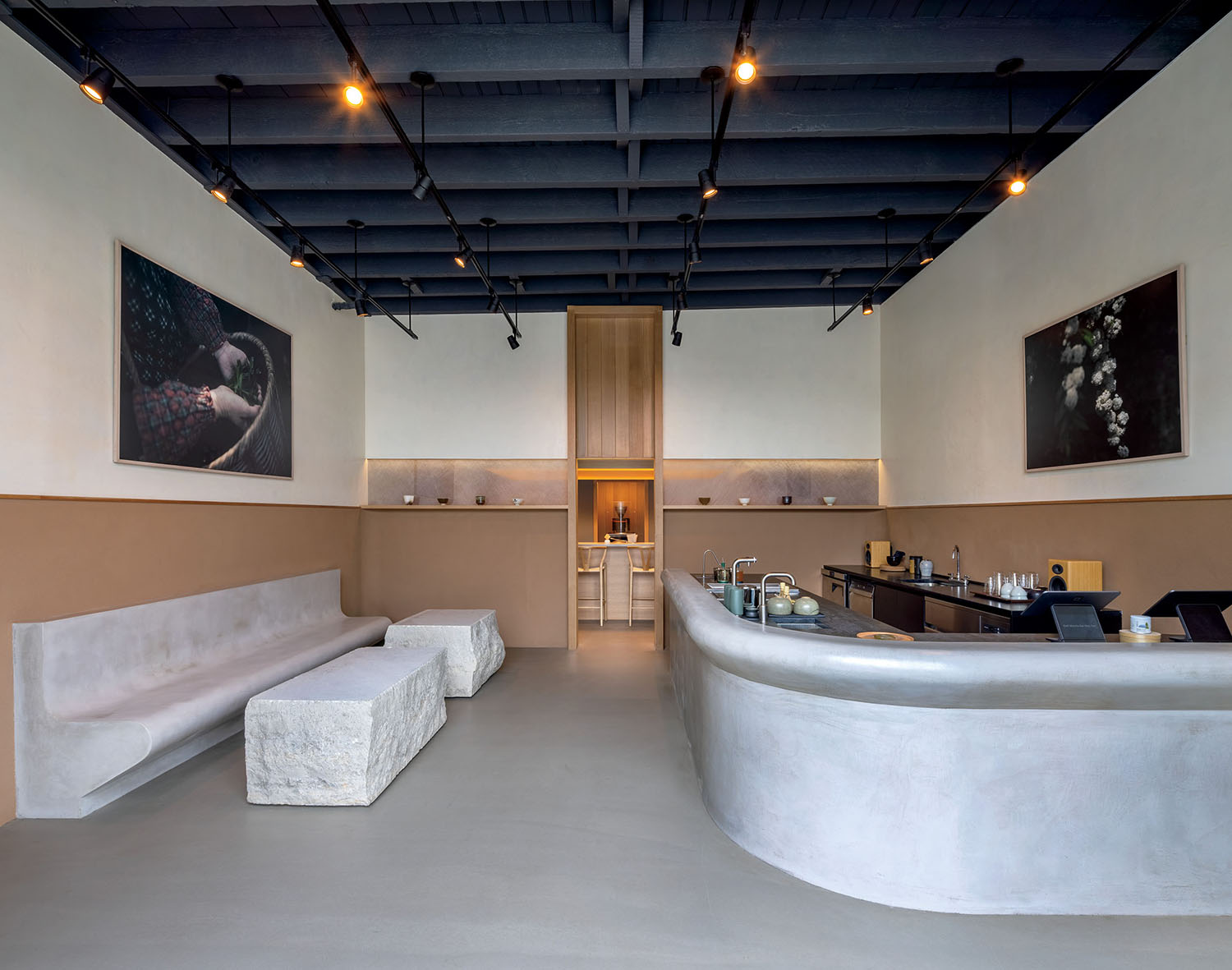 Modern coffee shop interior with stone benches, a curved service counter, and two framed prints on the walls.