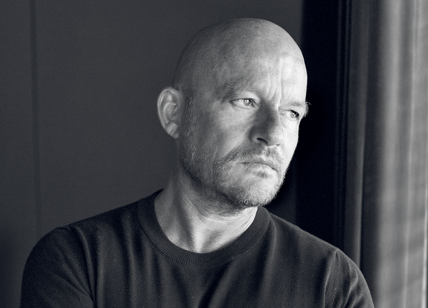 Black and white portrait of a bald man with a beard, looking toward the side.